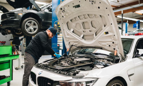 Mechanic at Bavarium Autoworks repairs vehicle A/C, checking refrigerant levels under the hood of a BMW.