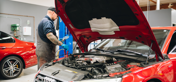 Auto mechanic at Bavarium Autoworks uses tool to check vehicle engine and battery health.