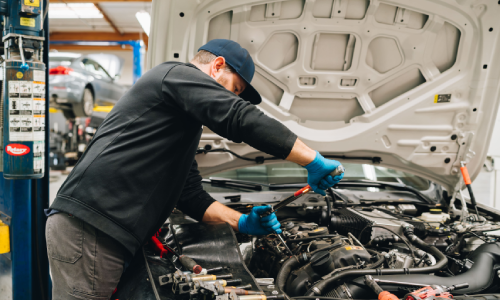 Auto technician performs diagnostic inspection on red Mercedes, taking notes on his findings on an electronic device.