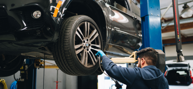 Mechanic in Mountain View, CA, performs tire repair on black BMW, checking the rims with gloved hands.
