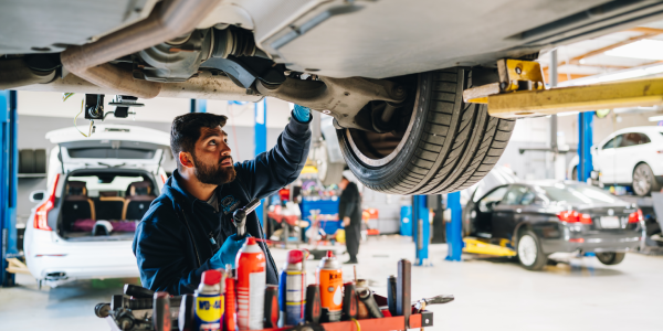 A European auto technician repairs oil leak from under the vehicle, using a variety of tools.