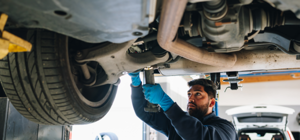 Auto technician inspects the undercarriage of vehicle, using a tool to make car repairs, Mountain View, CA.<br />
